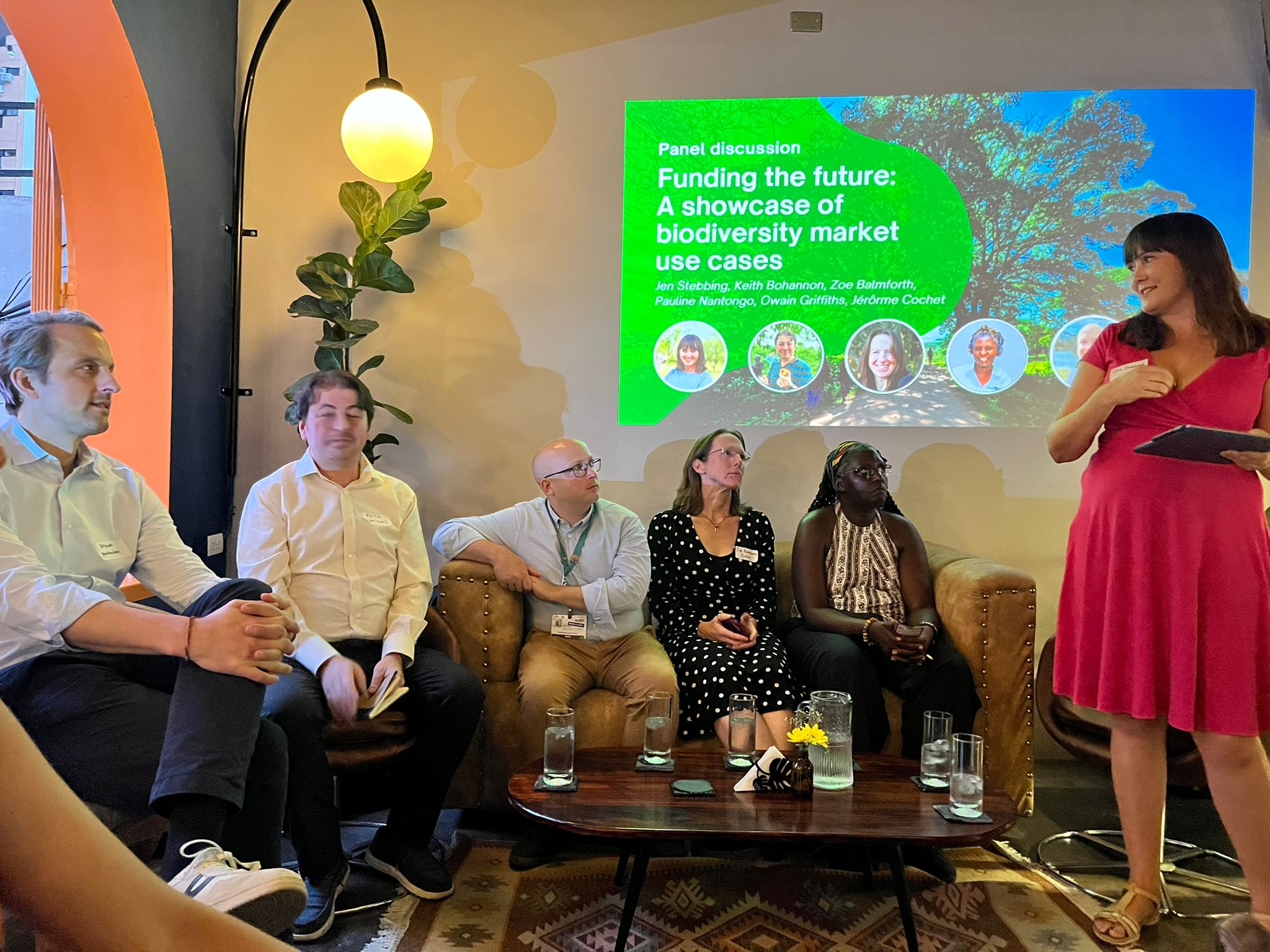 Jen Stebbing standing with a tablet, moderating a panel on biodiversity market use cases at COP16 in Cali