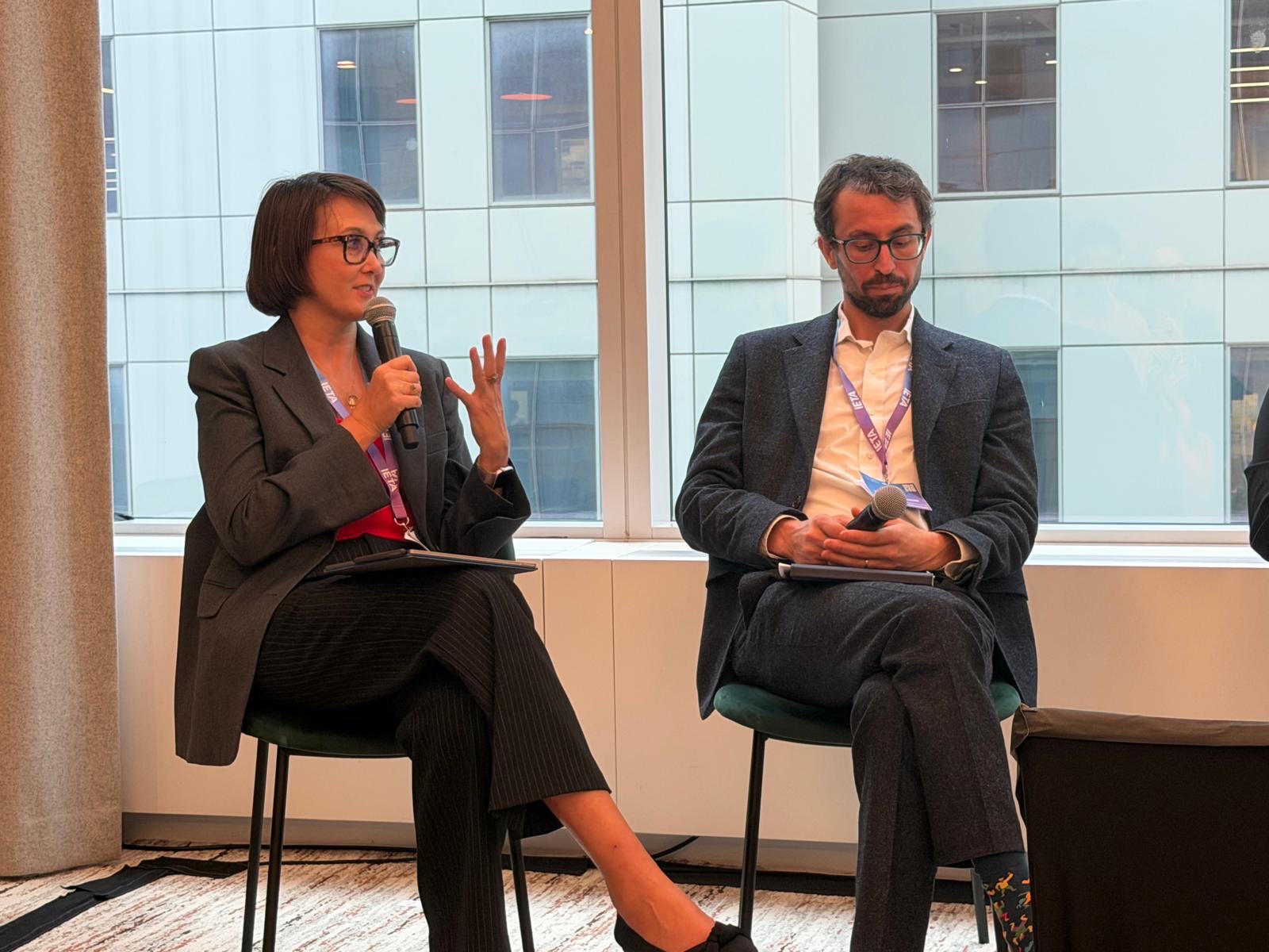 Two speakers seated in front of office windows, one speaking into a microphone, Climate Week NYC