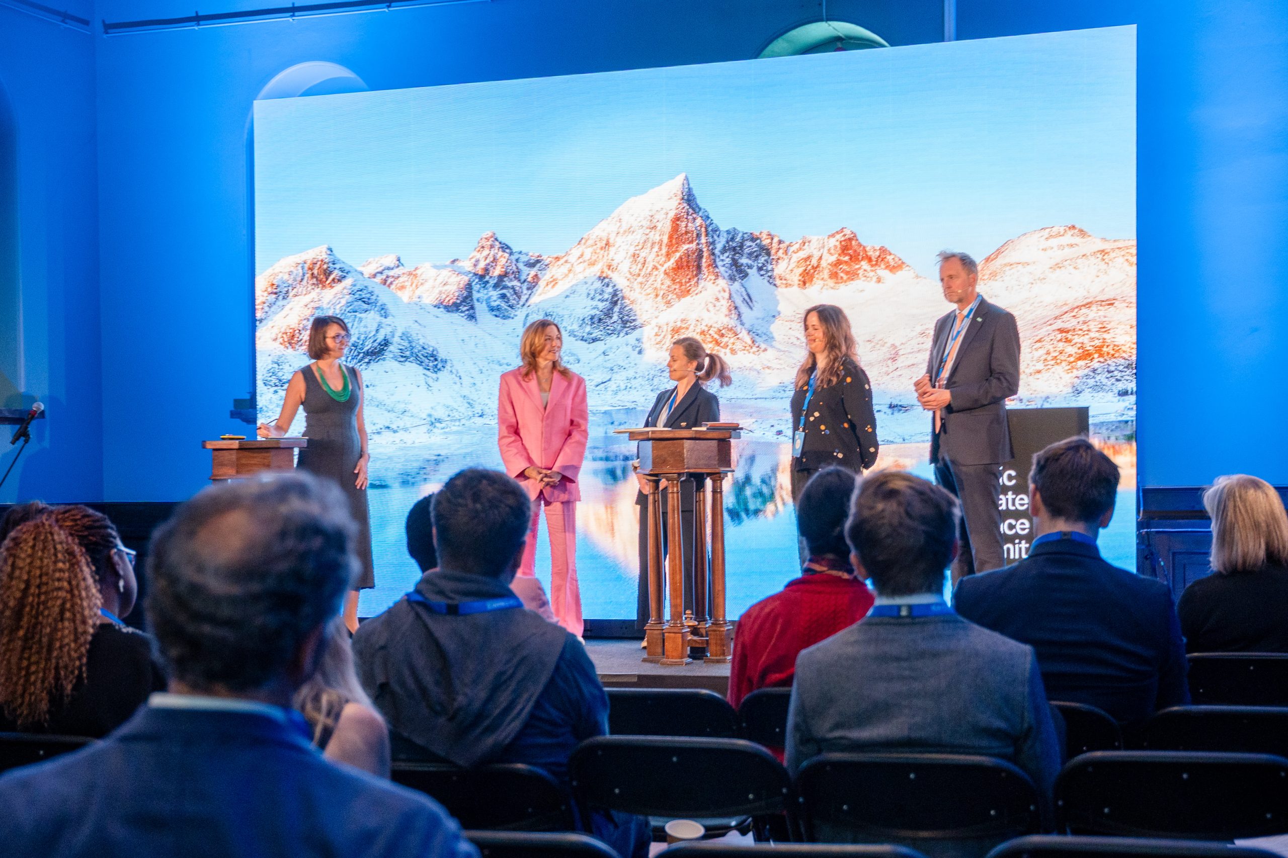 Five speakers standing on stage in front of a snowy mountain backdrop at the Nordic Climate Finance Summit, Oslo