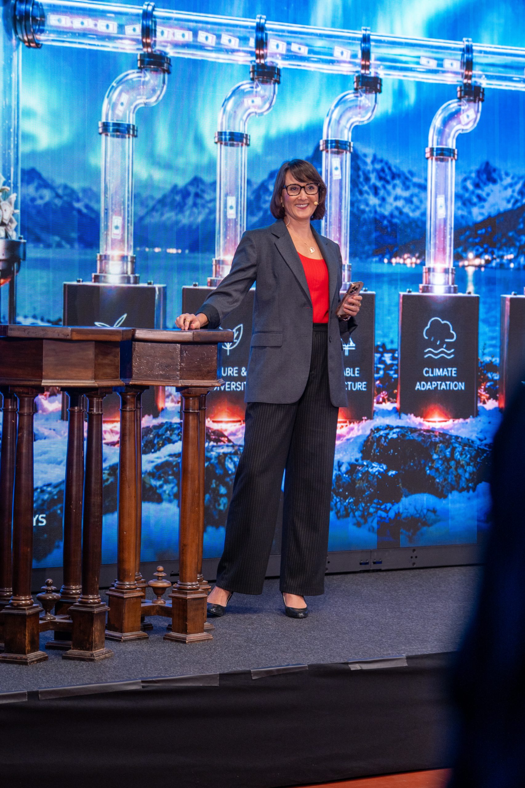 Jen Stebbing hosting the Nordic Climate Finance Summit in Oslo, standing on stage beside a wooden lectern