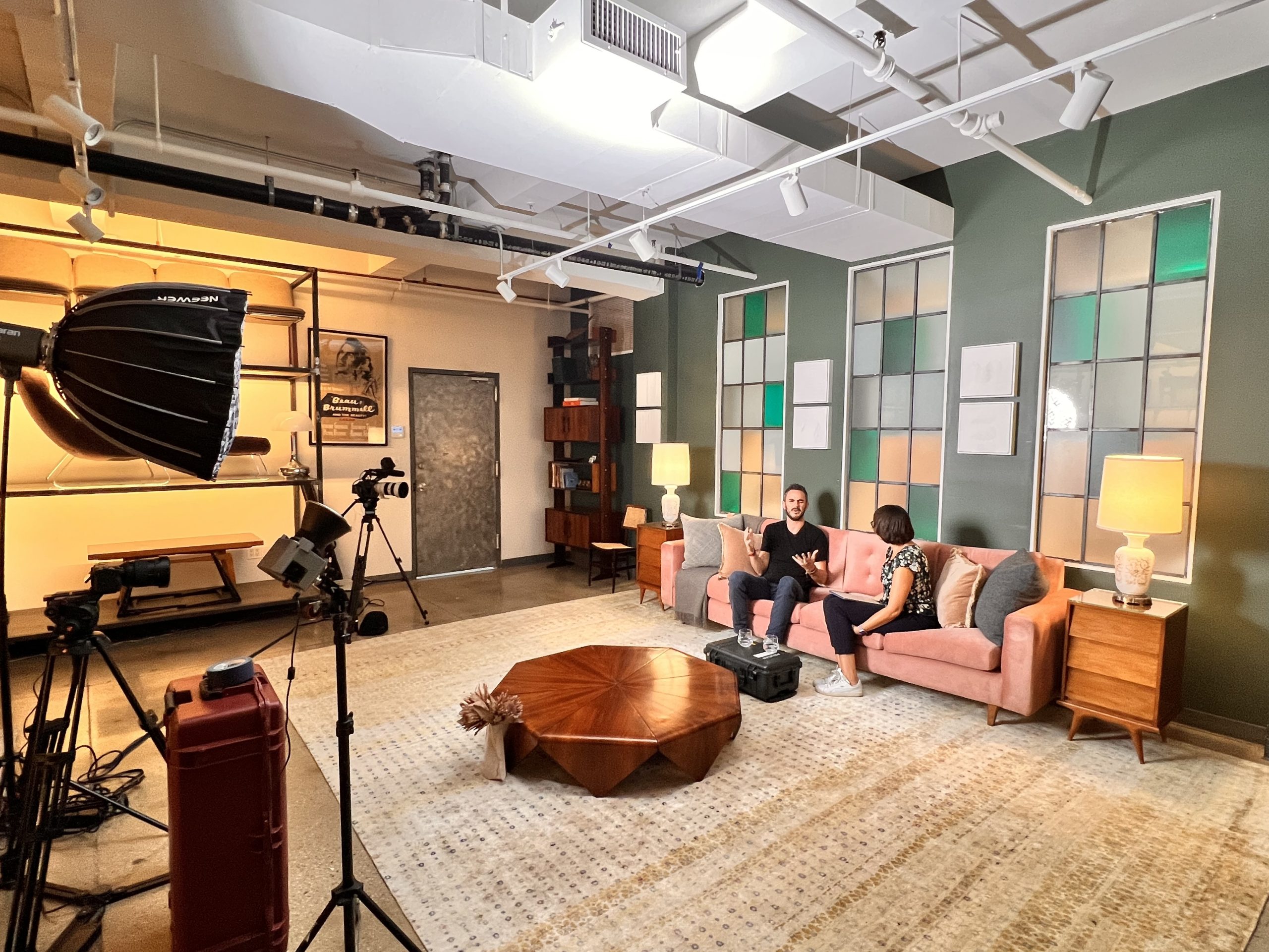 Two people in conversation on a pink sofa in a lit film studio, cameras in the foreground, Climate Week NYC