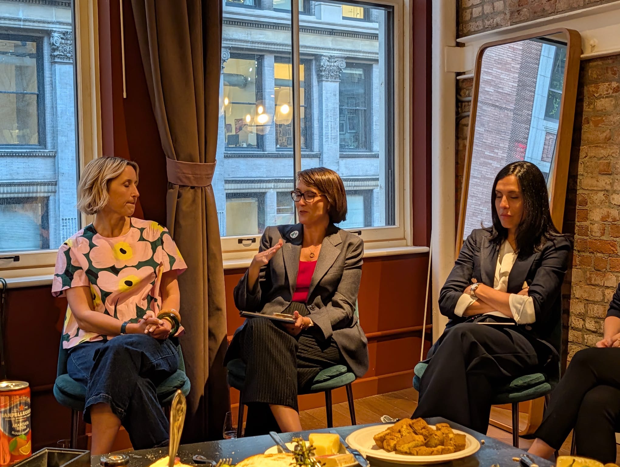 Three speakers seated by a tall window, one holding a microphone, at a Climate Week NYC session